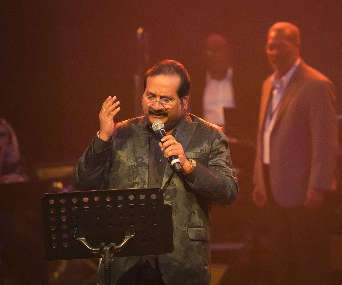 Mano singing on stage under warm light at Mano Live in Concert